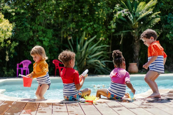 4 enfants avec des tee-shirts anti-noyade enfant jouant près de l'eau
