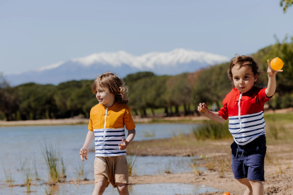 deux enfants au bord d'un lac, portant des tee-shirts anti-noyade Floatee jaune et rouge