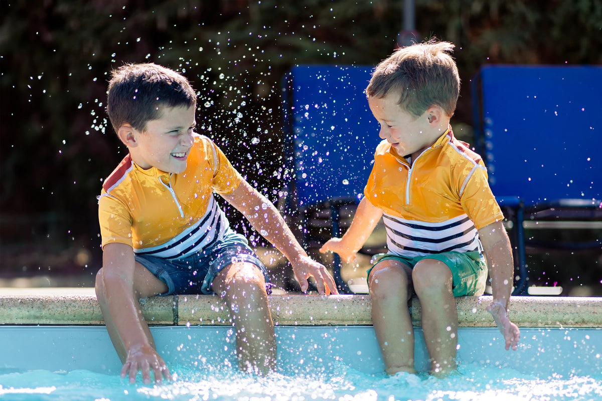 Deux enfants garçons jouent à s'éclabousser au bord d'une piscine, en portant le tee-shirt anti-noyade Floatee, manches courtes, marinière en bas et jaune en haut