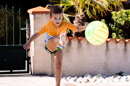 Enfant garçon jouant au ballon tout en portant le tee-shirt anti-noyade Floatee, manches courtes, marinière en bas et jaune en haut