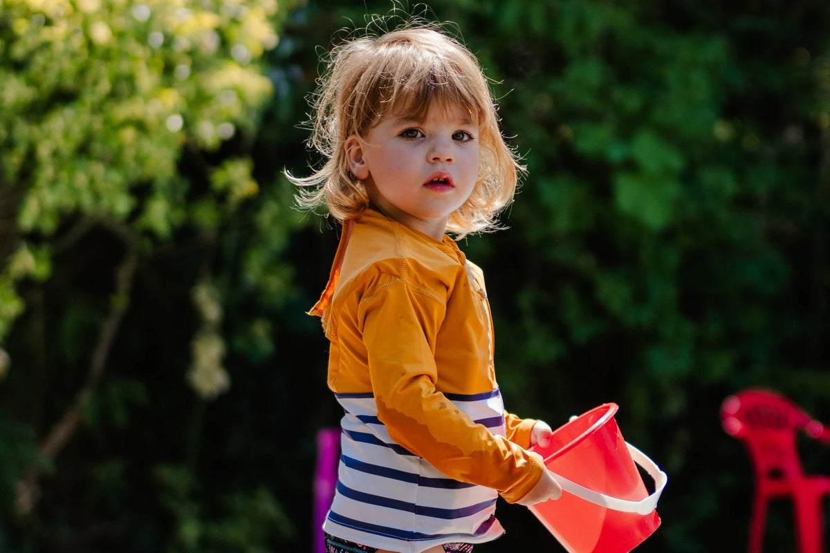 Enfant fille portant un seau pour jouer et ayant sur elle le tee-shirt anti-noyade Floatee, manches longues, marnière en bas et jaune en haut