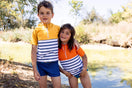 Deux enfants portent le tee-shirt anti-noyade Floatee, manches courtes, marinière en bas et couleur unie en haut (garçon : jaune, fille : orange)