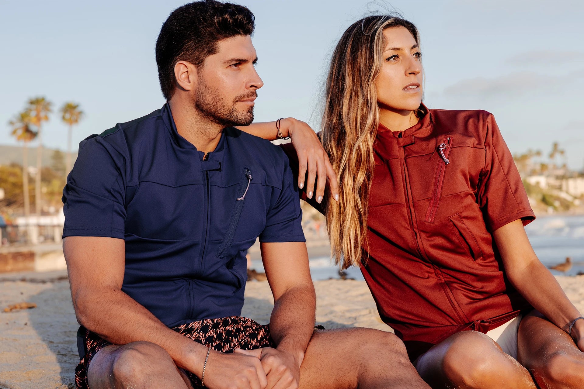 Homme et femme sur une plage et portant le tee-shirt anti-noyade adulte manuel Floatee, manches courtes, rouge pour la femme et bleu pour l'homme