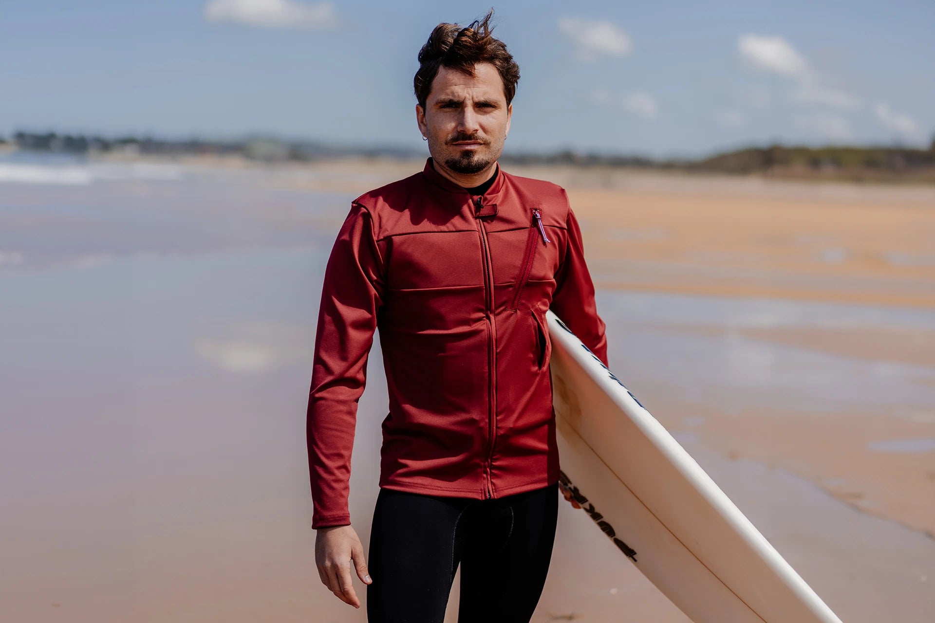 Homme sur une plage avec une planche de surf et portant le tee-shirt anti-noyade adulte manuel Floatee, manches longues, rouge