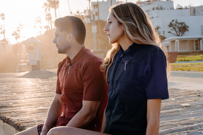 Homme et femme en bord de plage et portant le tee-shirt anti-noyade adulte manuel Floatee, manches courtes, bleu pour la femme et rouge pour l'homme