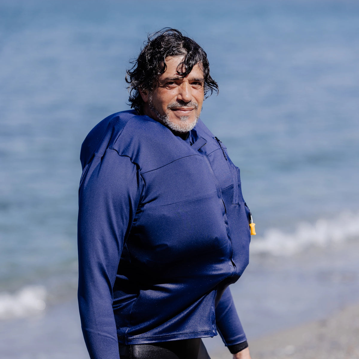 homme sur une plage portant un T-shirt anti-noyade Floatee bleu à manches longues, gonflé