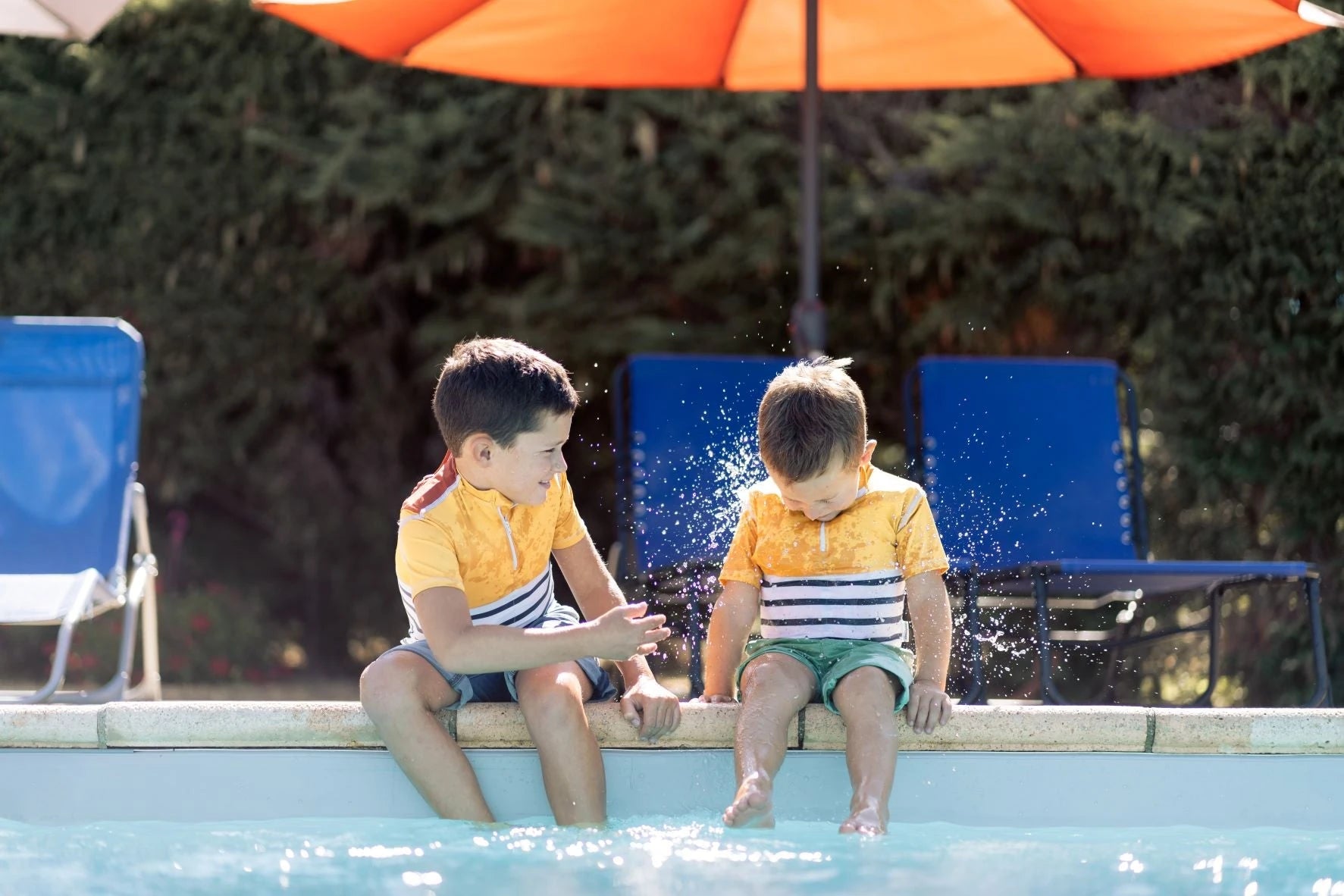 Floatee, le tee-shirt anti-noyade pour enfant, ne se déclenche qu'en cas d'immersion et pas en cas d'aspersion, comme le montrent 2 enfants qui s'éclaboussent au bord de la piscine