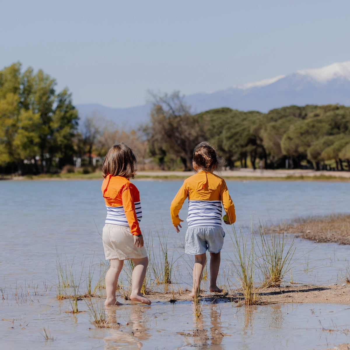 deux enfants au bord d'un plan d'eau, portant des tee-shirts anti-noyade Floatee jaune et orange
