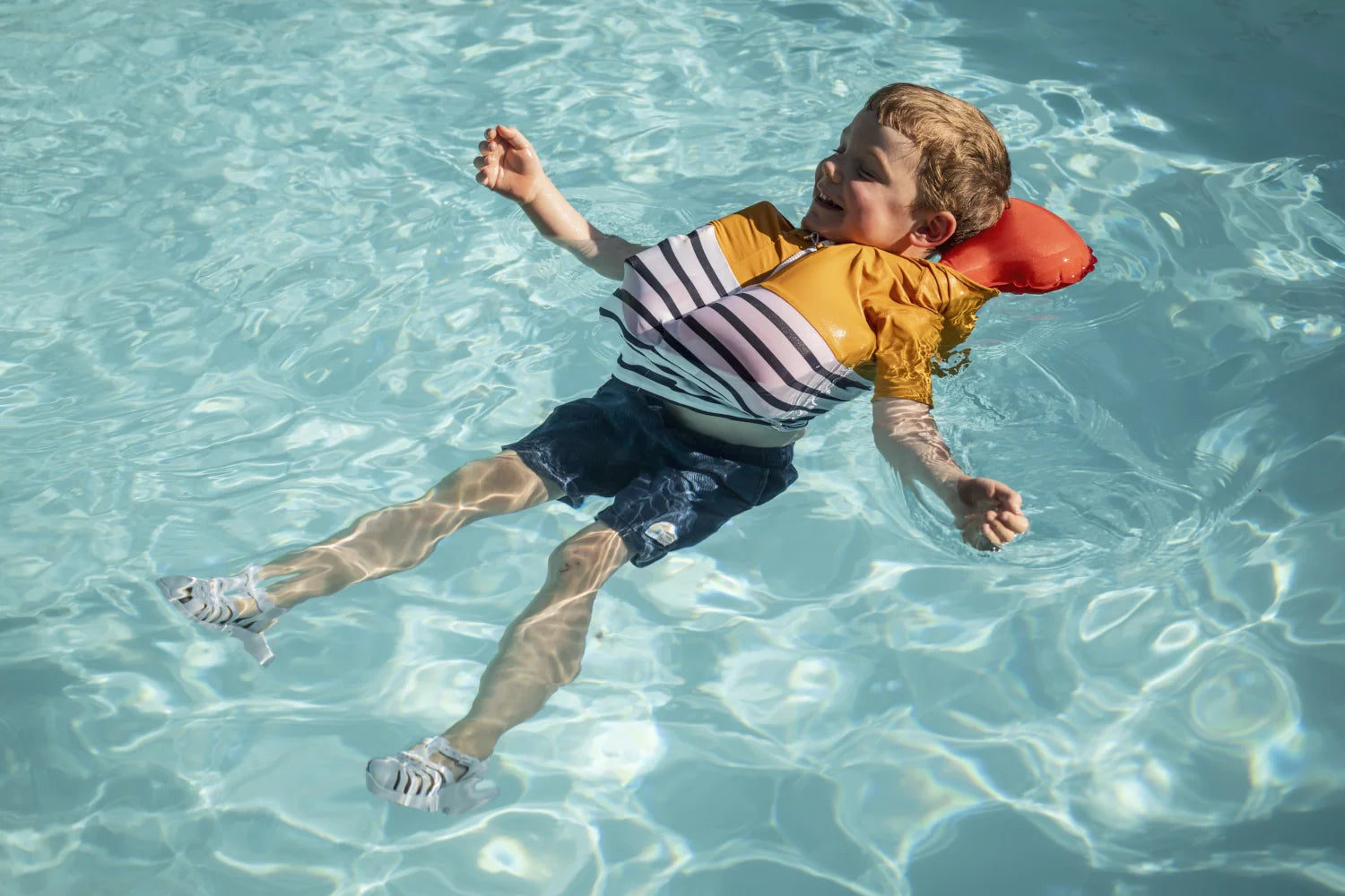 Enfant dans une piscine portant le tee-shirt anti-noyade Floatee, jaune et manches courtes, avec le dispositif de sauvetage gonflé