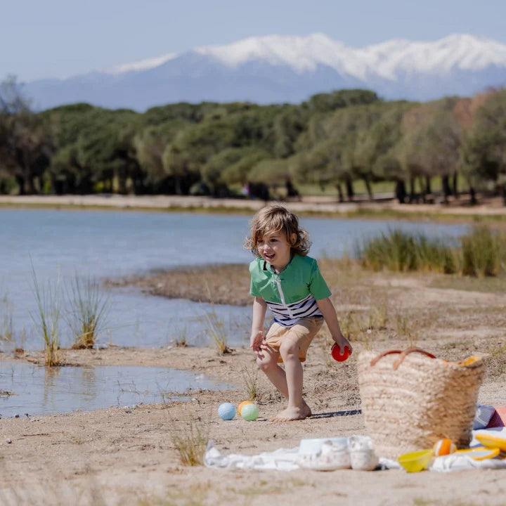 enfant portant le Tee-shirt anti-noyade enfant Floatee vert, jouant à la pétanque au bord d'un lac, image format carré