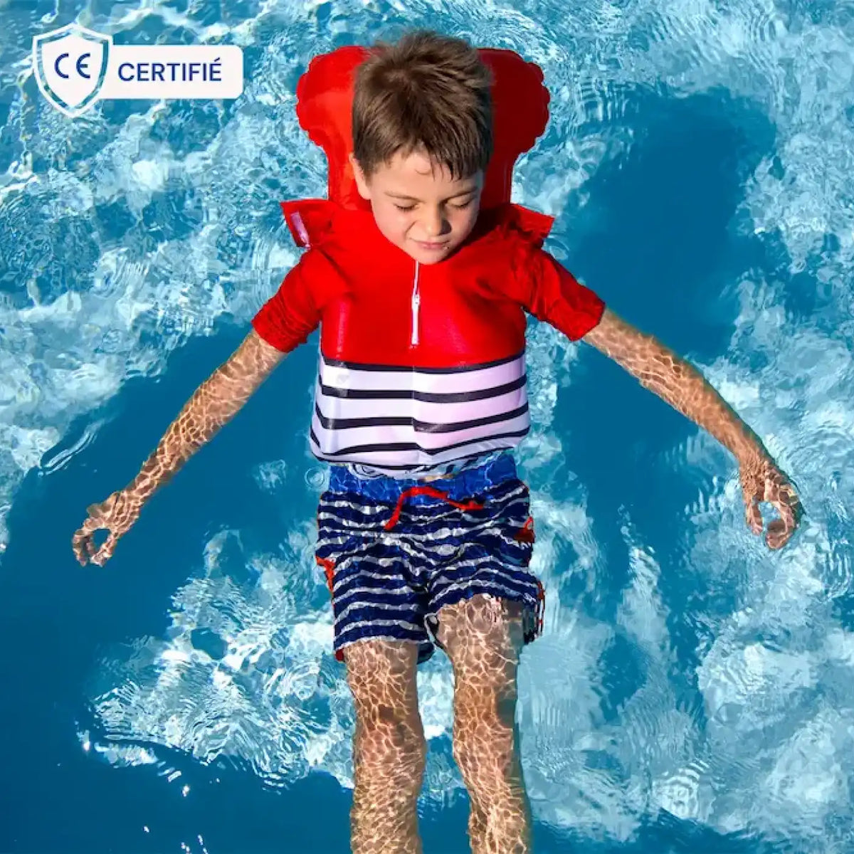 un petit garçon dans l'eau portant un tee-shirt anti-noyade rouge manches courtes gonflé